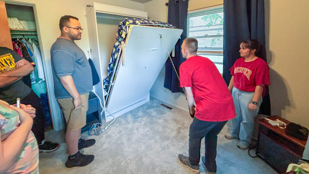 Brandon, a Heartspring Pediatric Outpatient Clinic client, pulls the handle for his Murphy bed to lower the bed as WSU engineering students who created the solution observe his pogress.