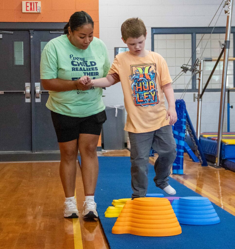 Heartspring Therapeutic School paraprofessional helps a student navigate stepping stones in adaptive gymnastics at the YMCA.